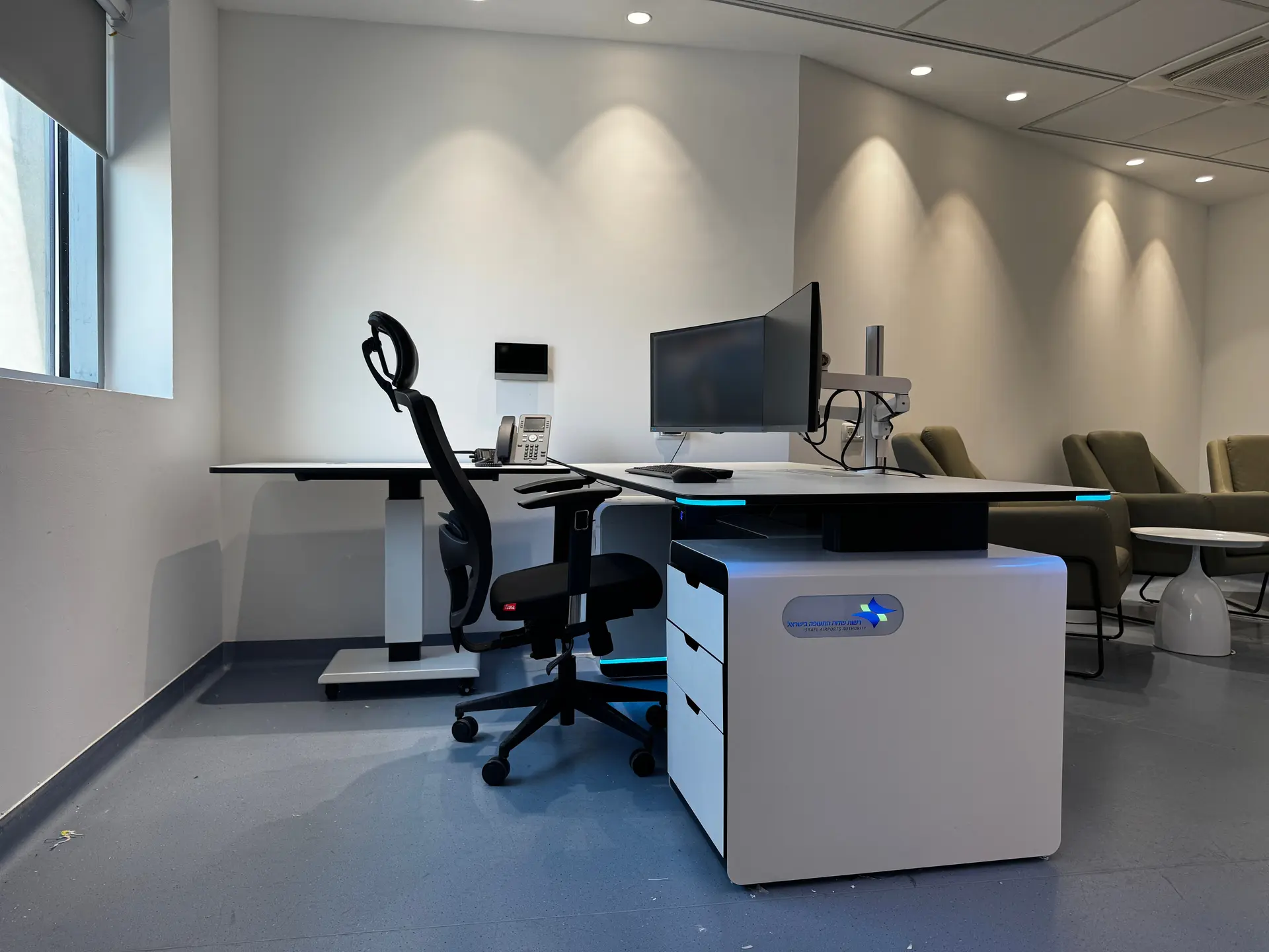 Side view of a workstation with monitor arms, a chair, drawer unit and integrated lighting